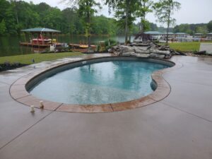 a custom inground vinyl swimming pool from Kirk's Pool and Hearth in the foreground, with trees and a lake in the background