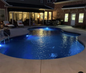 a custom inground vinyl pool from Kirk's Pool and Hearth, pictured at night with lights shining below the water