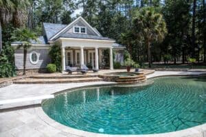 a beautiful curved fiberglass pool with a diving board that ripples with sunlight. A columned house is in the background