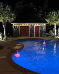 a custom inground vinyl swimming pool from Kirk's Pool and Hearth, lit up from the bottom at night time. Inflatable flamingos float on the surface