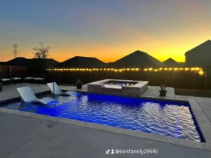 a rippling vinyl inground pool installed by Kirk's Pool and Hearth. the sun is setting behind some houses and trees in the background