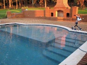 One of Kirk's Pool and Hearth's vinyl inground pools. It has a custom design and inset steps, pictured at sunset.