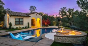 a beautiful vinyl pool from Kirk's Pool and Hearth at sunset, while a fire pit lights up on the right side of the frame